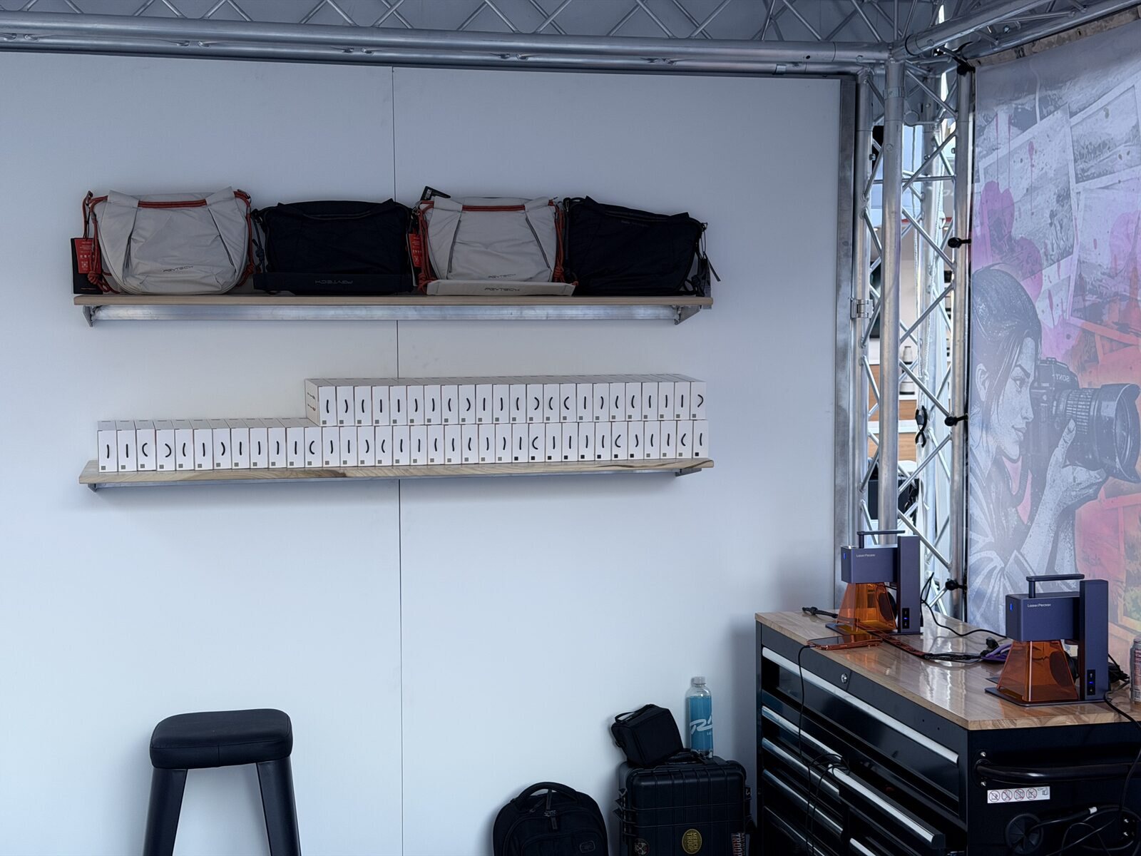 Back wall of an event station with shelved blank bags and boxed stock ready for guests